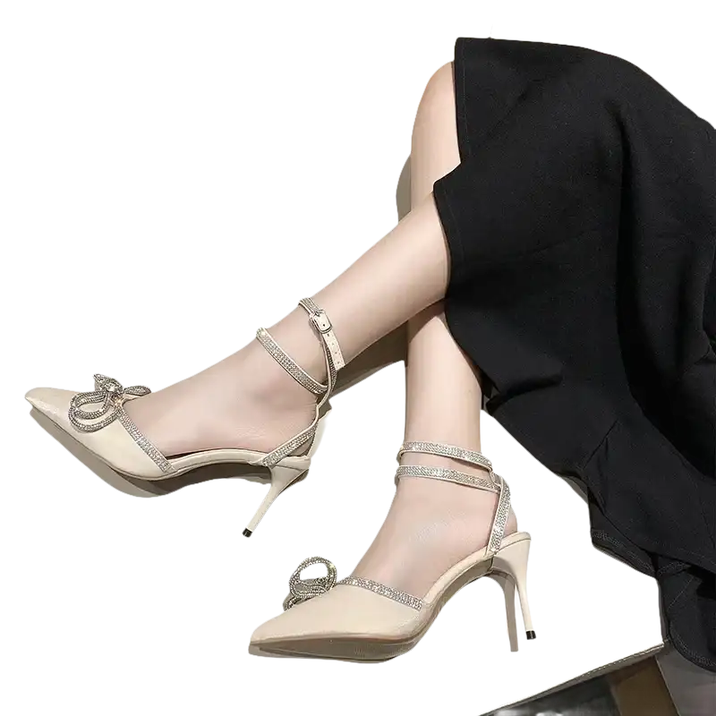 Beige high-heeled shoes with rhinestone straps and bow.