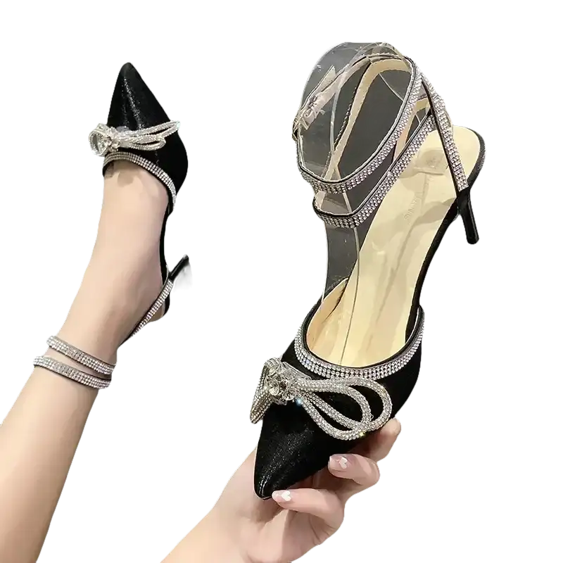 Black high-heeled shoe with rhinestone bow and ankle straps.