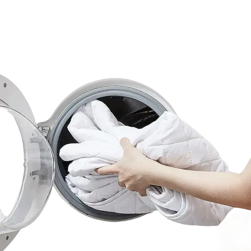 White quilted blanket being loaded into a washing machine.