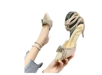 Beige high-heeled shoes with rhinestone bows and ankle straps.
