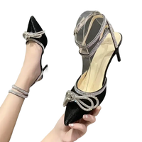 Black high-heeled shoe with rhinestone bow and ankle straps.