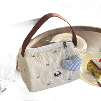 Quilted cream-colored handbag with brown handle and heart-shaped charm.