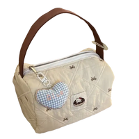 Quilted cream-colored handbag with brown handle and heart-shaped charm.