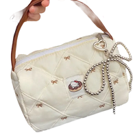Quilted cream-colored handbag with brown handle and beaded bow.