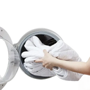 White quilted blanket being loaded into a washing machine.