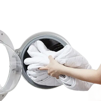 White quilted blanket being loaded into a washing machine.